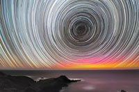 چرخش شبانگاهي ستاره ها و درخشش شفقهاي قطبي بر فراز افق در استراليا. شفقهاي قطبي زماني بوجود ميآيند كه ذرات باردار خورشيد با سرعت زياد با جو زمين برخورد ميكنند.